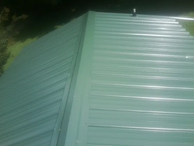 New green metal panels meeting at the ridge of a roof — Flat Roof Repair work by our crew in Jasper