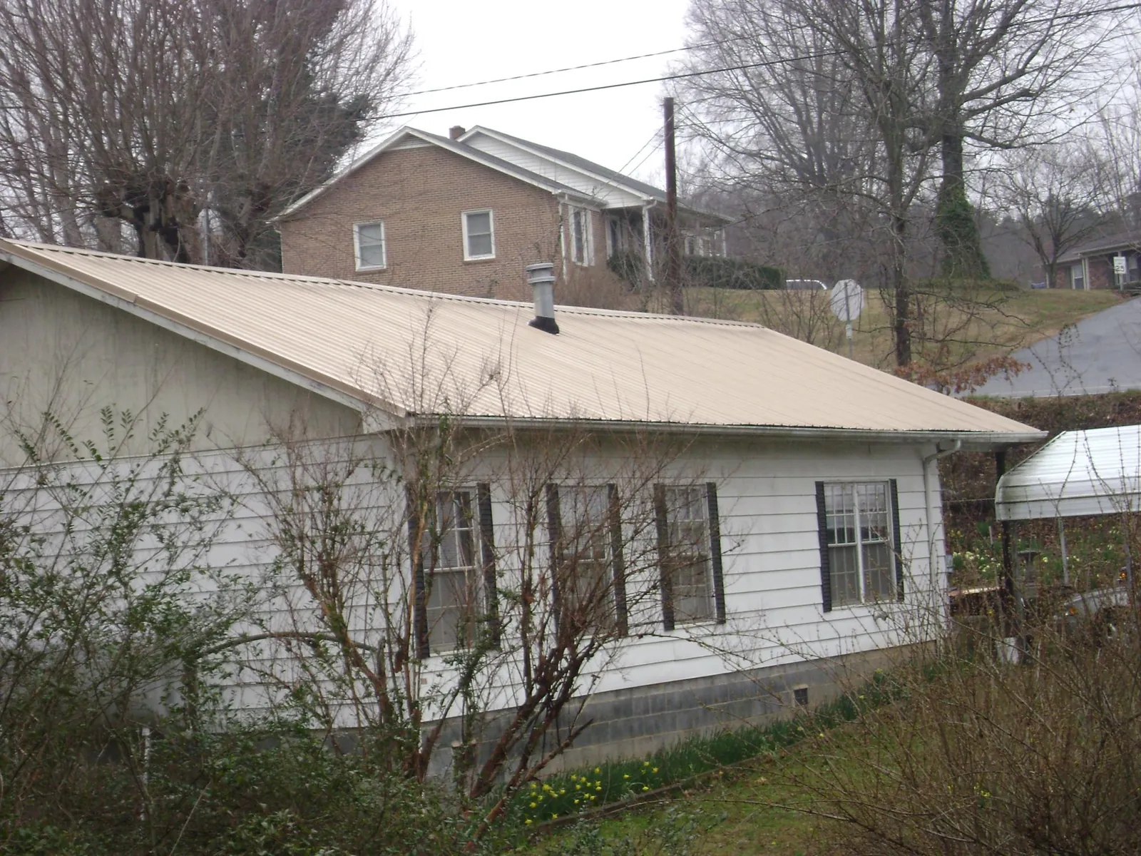 Tan metal roof on a white sided house set into a hillside — Commercial Roofing by Roofing Brothers in Jasper